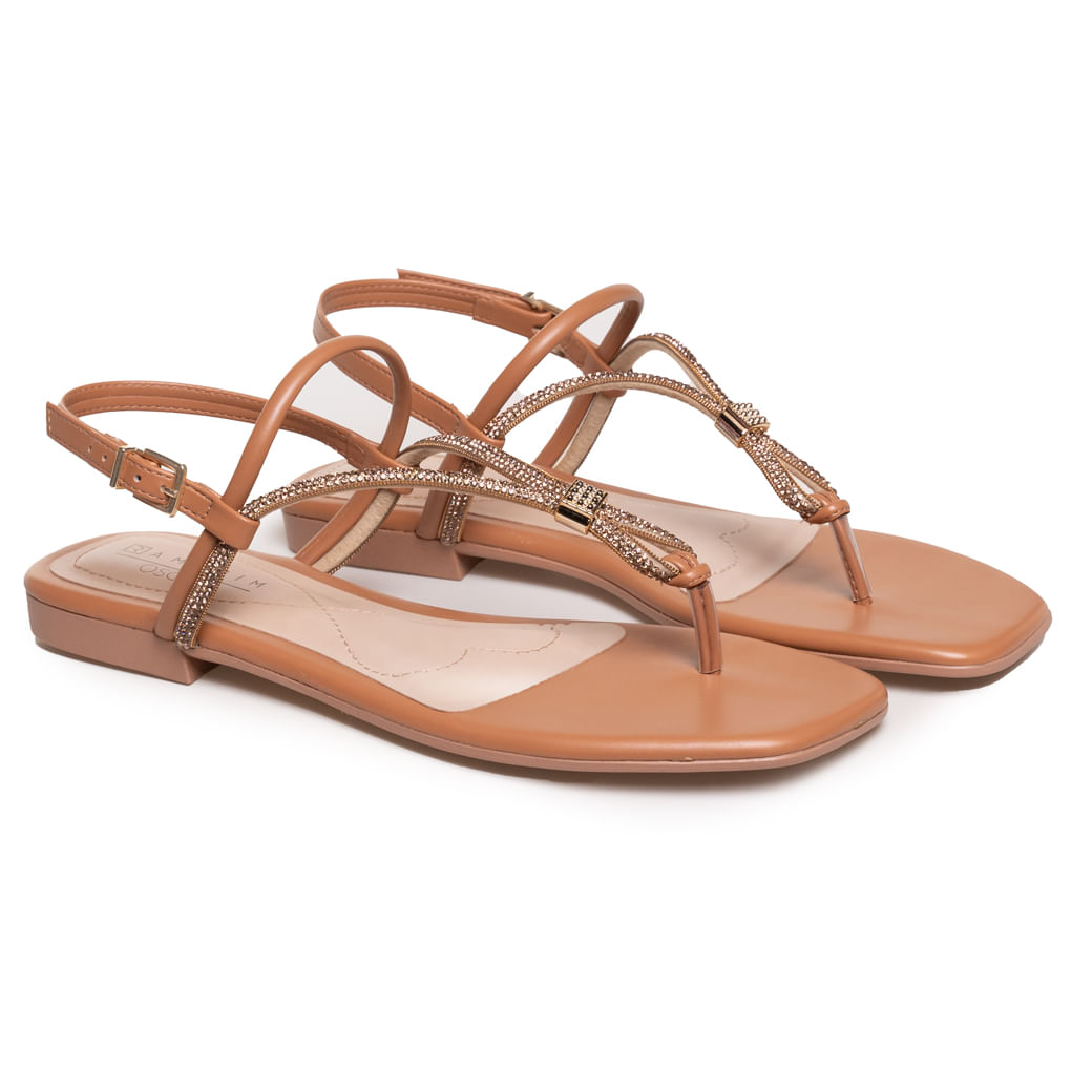 Par de sandálias rasteiras marrom com tiras em T e strass dourado sobre fundo branco