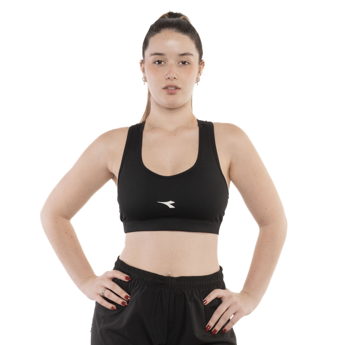 Top esportivo feminino Diadora preto com decote em V e logo branco, usado por mulher sorridente com braços cruzados