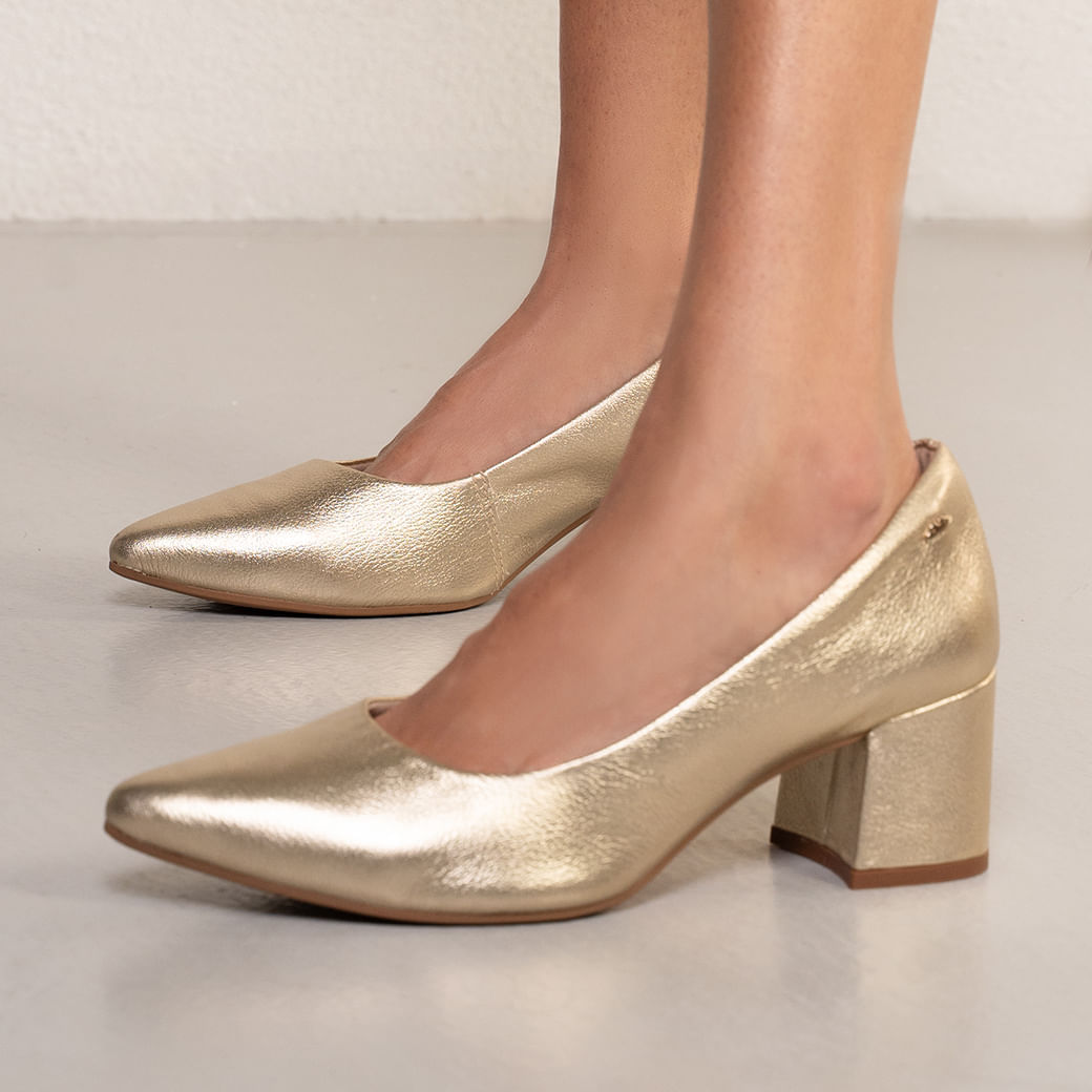 Close lateral do scarpin dourado mostrando bico pontiagudo e textura metalizada