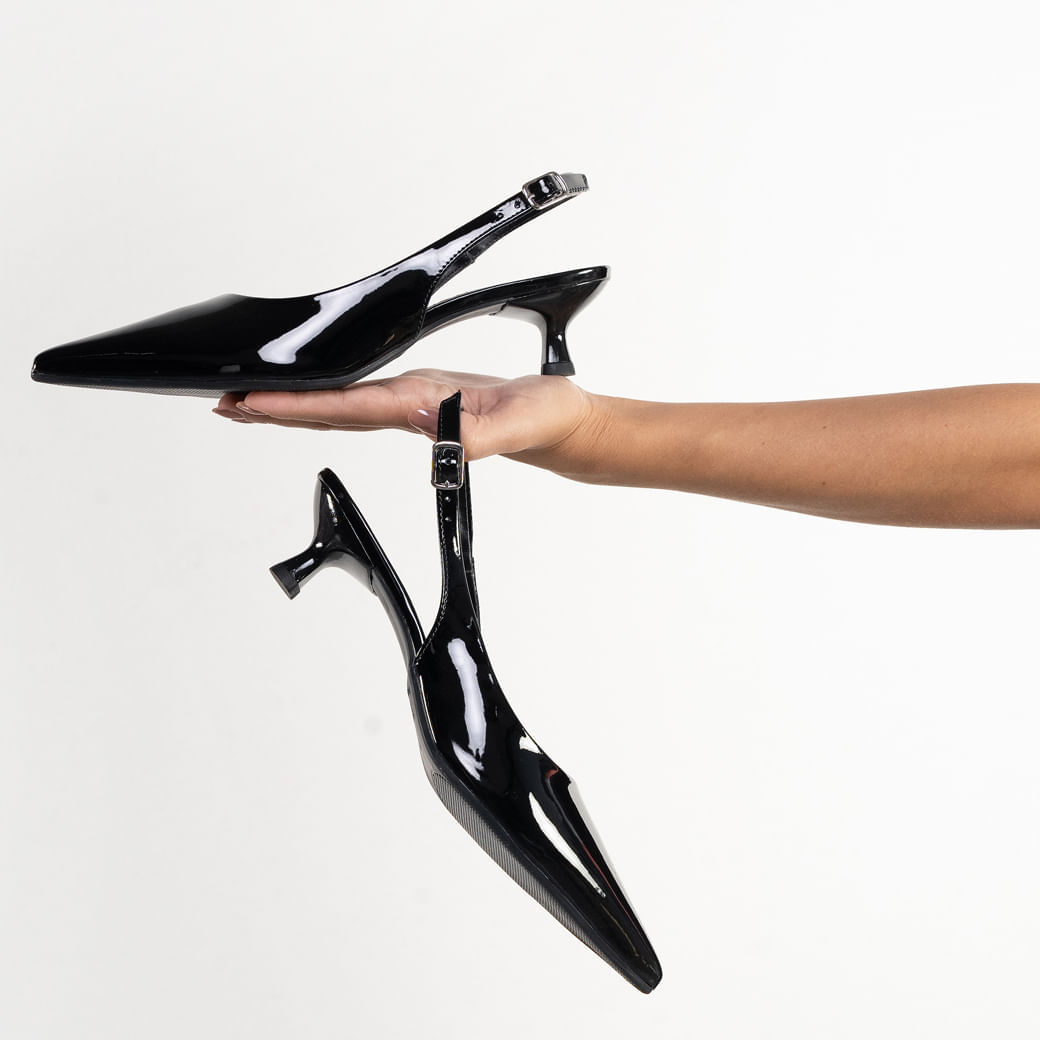 Sapato scarpin preto verniz com salto fino usado por pessoa sentada