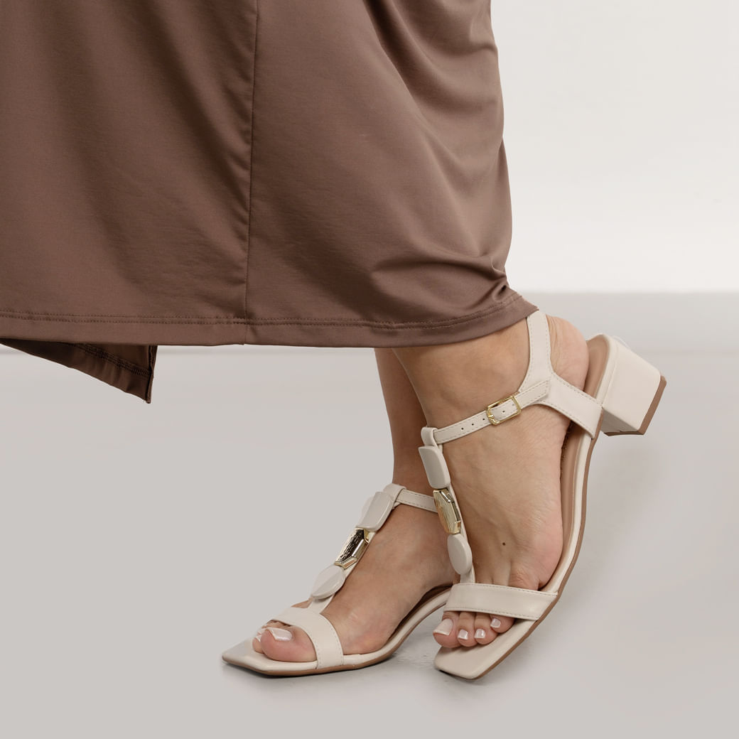 Vista lateral da sandália feminina off white com salto bloco e detalhes em fivela dourada.