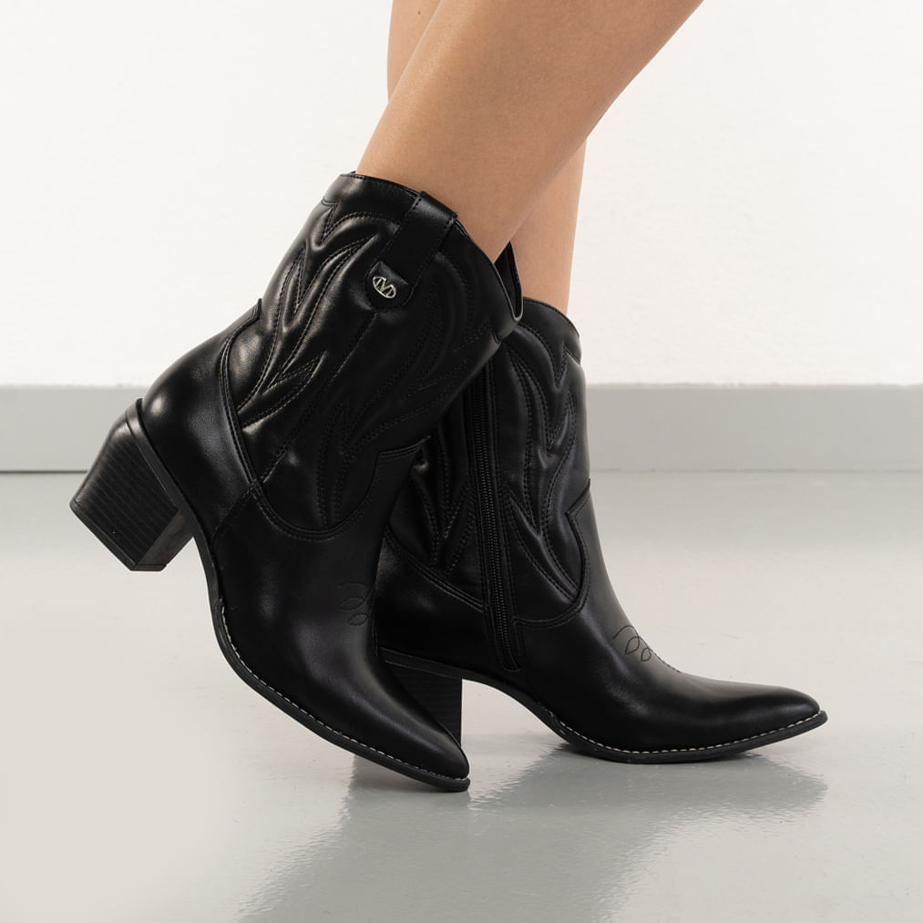 Mulher usando bota preta Via Marte cano baixo com vestido preto, mostrando o conforto e estilo