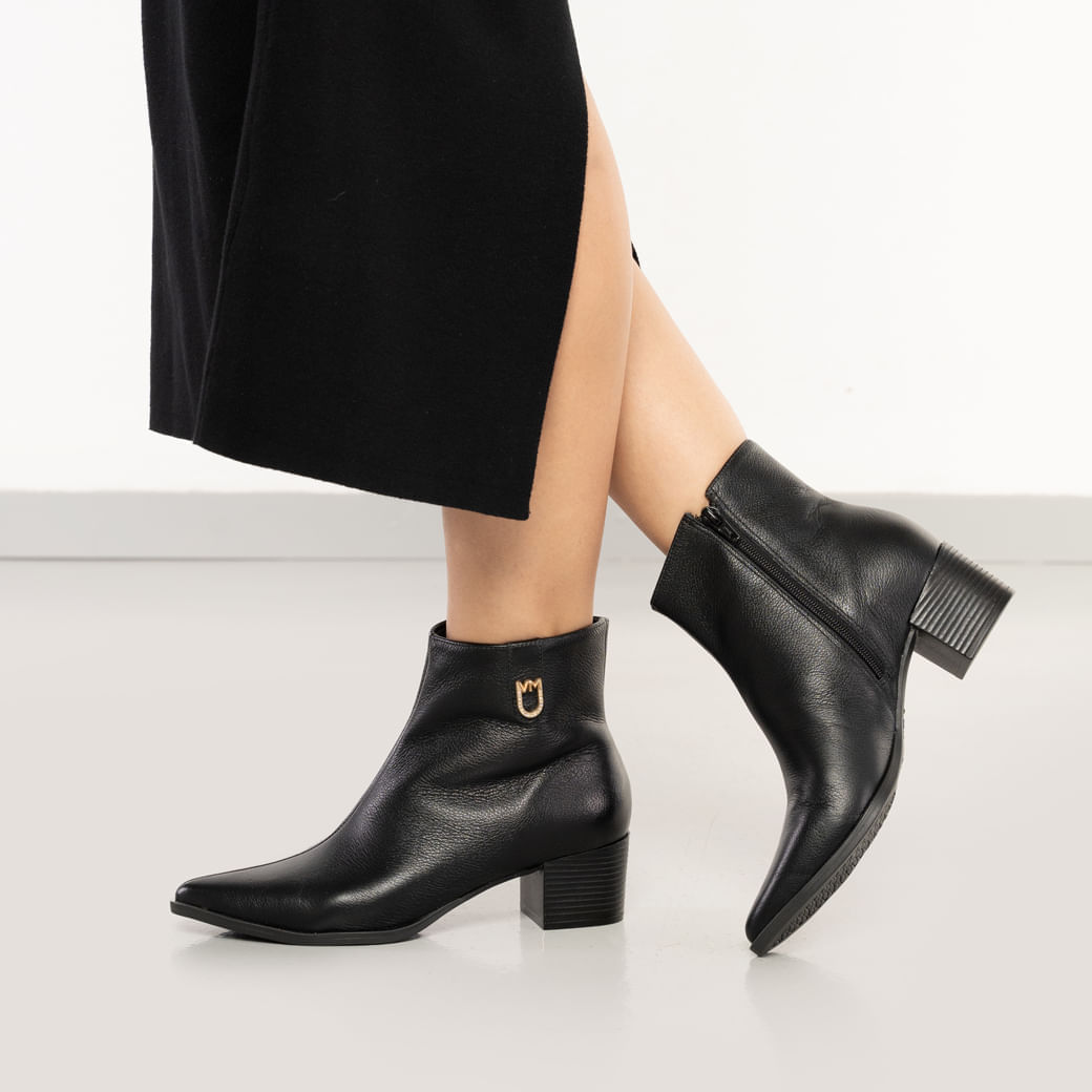 Vista lateral da bota feminina preta de couro legítimo com salto grosso e detalhes em fivela dourada