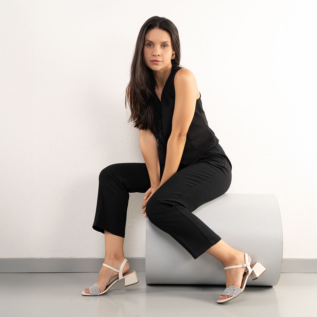 Modelo usando sandália off white com tira frontal em brilho e salto bloco médio, vista lateral