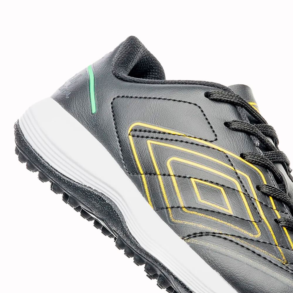 Close no cabedal da chuteira society preta Umbro com detalhes em amarelo