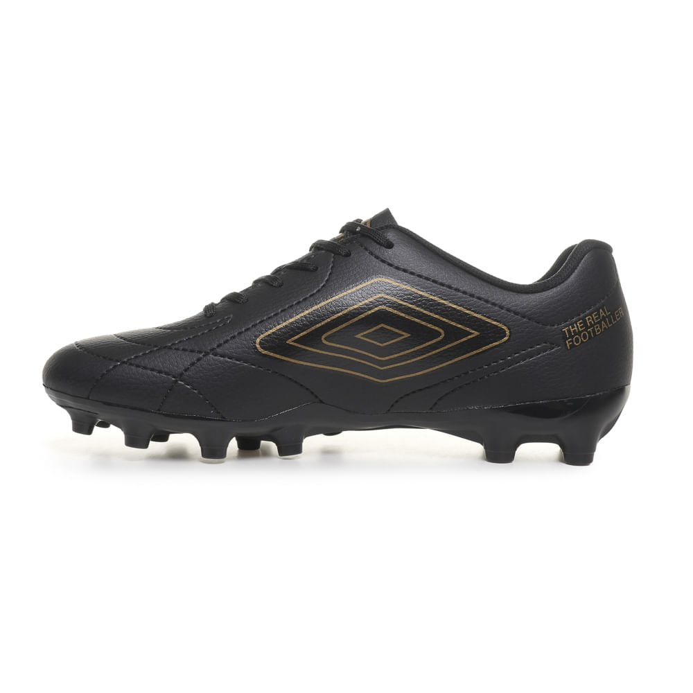Chuteira preta Umbro vista lateral esquerda destacando logo dourado e solado com travas para campo natural.