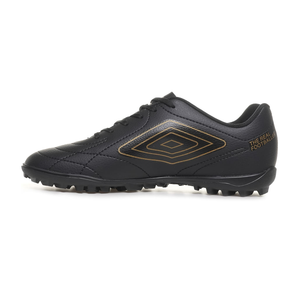 Perfil lateral esquerda da chuteira society Umbro preta com logo dourado e solado antiderrapante