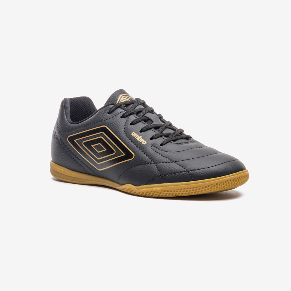 Chuteira futsal Umbro masculina preta com detalhes dourados vista frontal 3/4, mostrando cadarços e design texturizado.