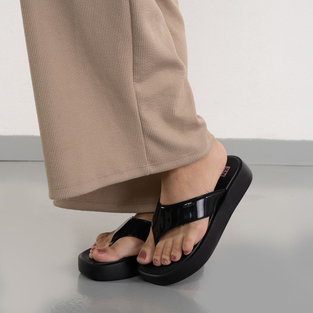 Tamanco anabela preto feminino de PVC sendo usado com calça bege clara