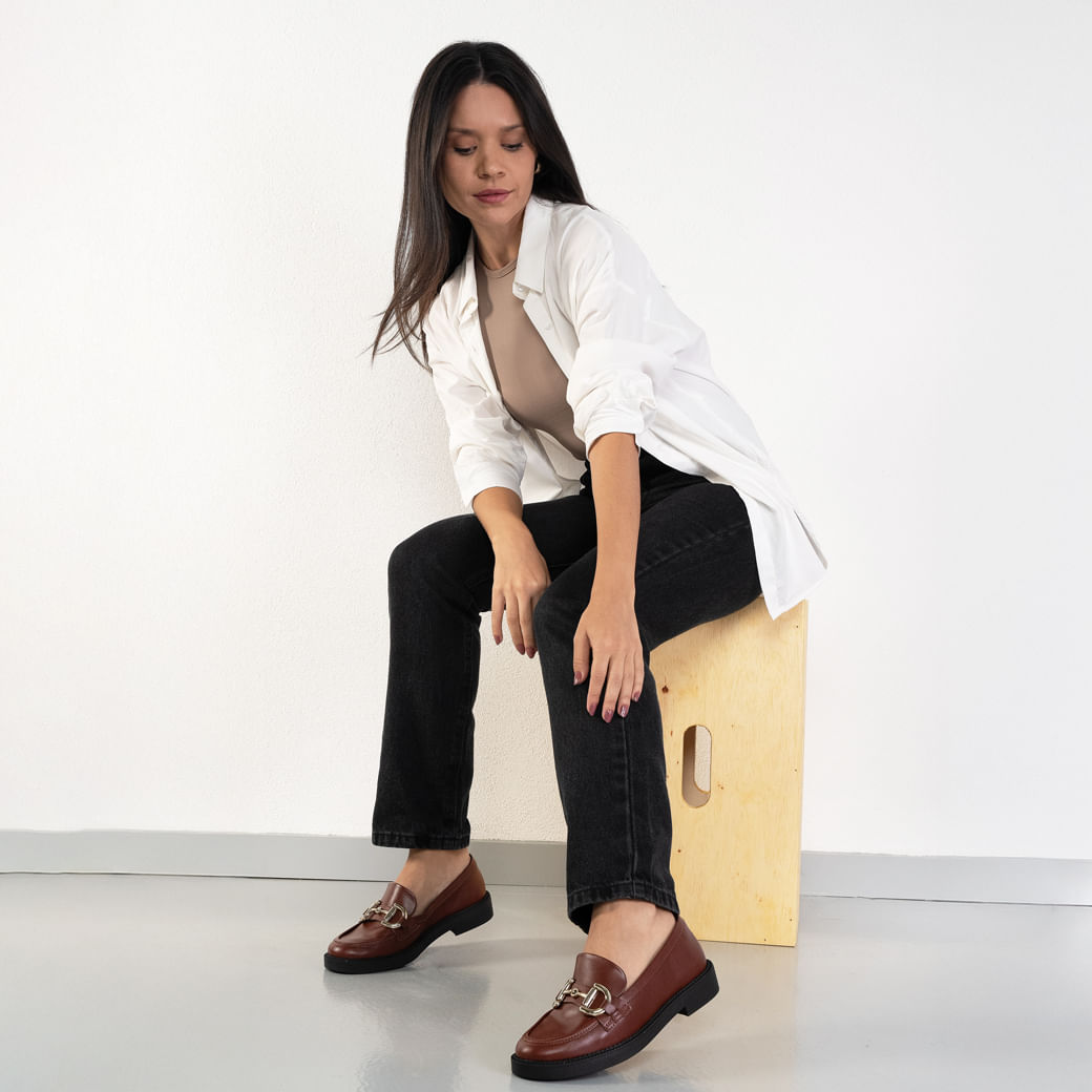Mocassim feminino marrom usado por modelo sentado, destaque no ajuste e acabamento
