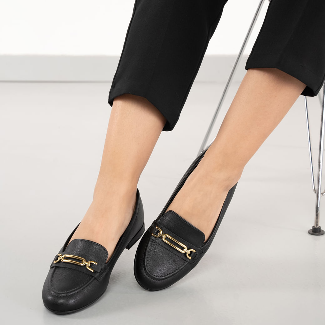 Mocassim Modare preto com detalhe dourado, visto no pé de modelo, destacando caimento e acabamento