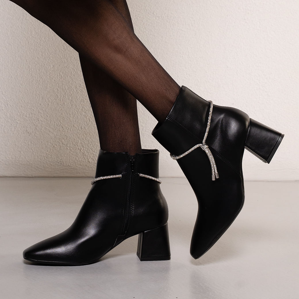 Close nas pernas com bota preta de salto grosso Vizzano mostrando o fechamento em zíper lateral