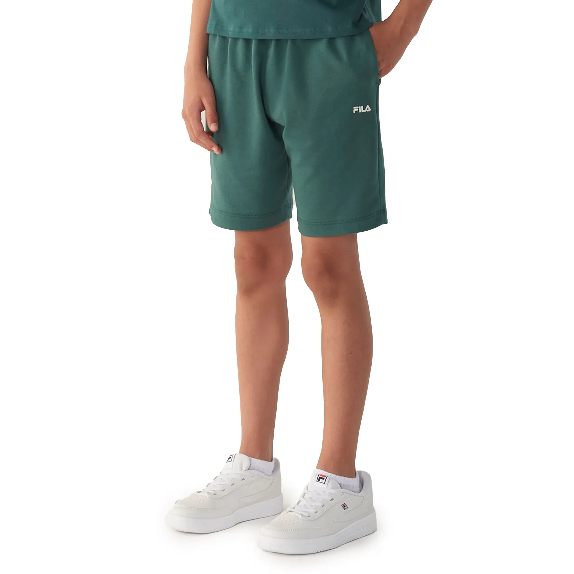 Bermuda infantil verde floresta FILA vista frontal com cós elástico e logo branco, usada por criança com tênis branco e camiseta verde.